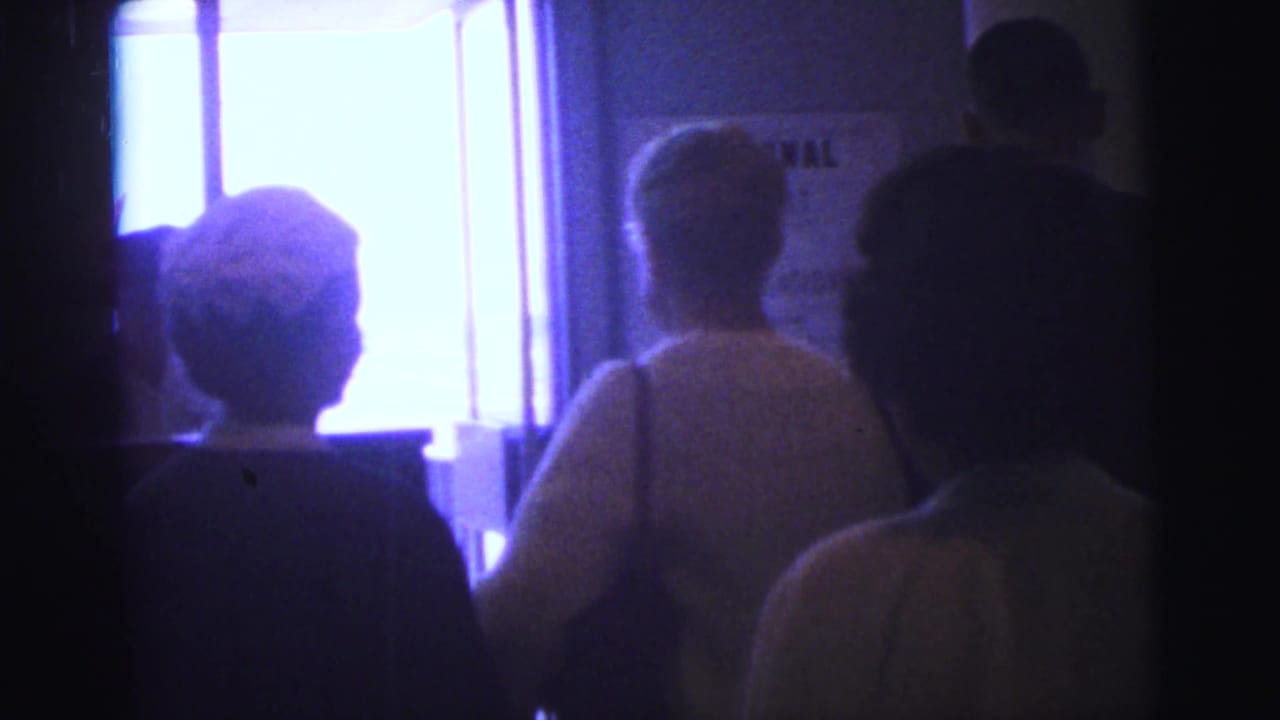 Travelers seen from behind near a bright doorway inside a terminal.