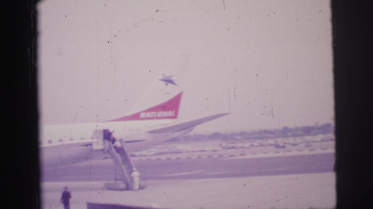 Passengers board a National Airlines plane by mobile stairs on an airport tarmac.