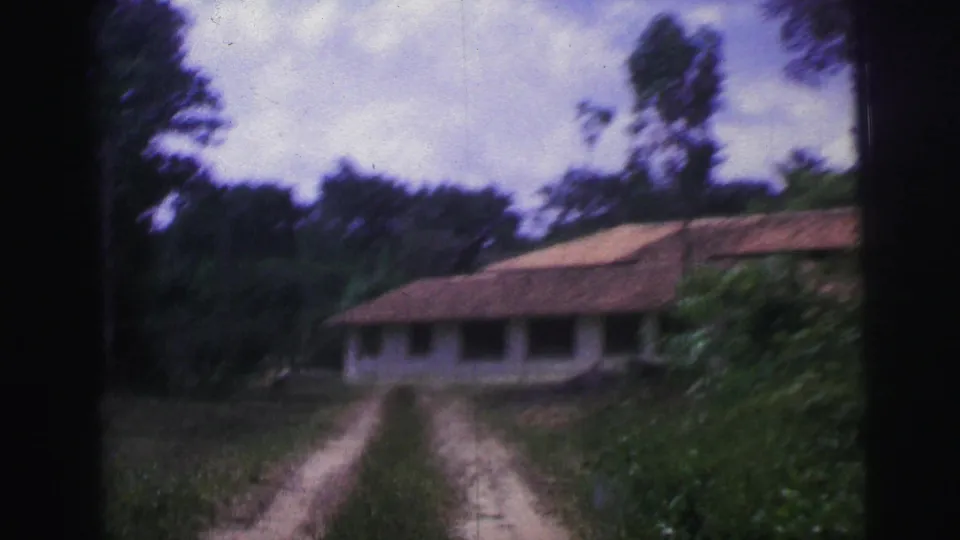 1967 Brazil 8mm frame with motion blur as the camera moves closer to a long tiled-roof house along a dirt driveway.