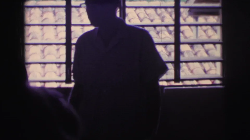 Interior 1967 Brazil 8mm frame showing a silhouetted standing figure against a barred window, with terracotta roof tiles visible outside.