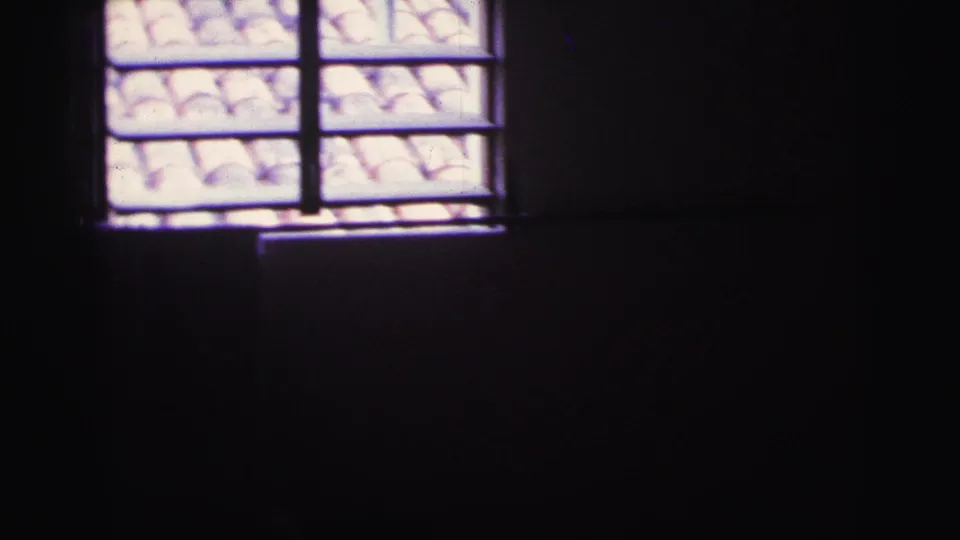 Dim 1967 Brazil interior with barred window sections and a tiled roof visible outside in bright light.