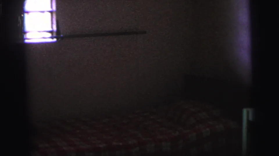 Sparse 1967 Brazil interior showing a small barred window, plain wall, and bed in low, grainy light.