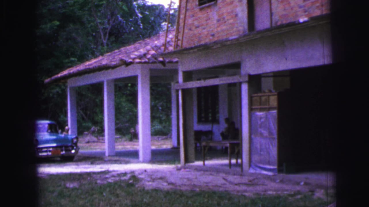 1967 Brazil frame with a turquoise sedan parked by a shaded villa porch, with people partly visible at the left edge.