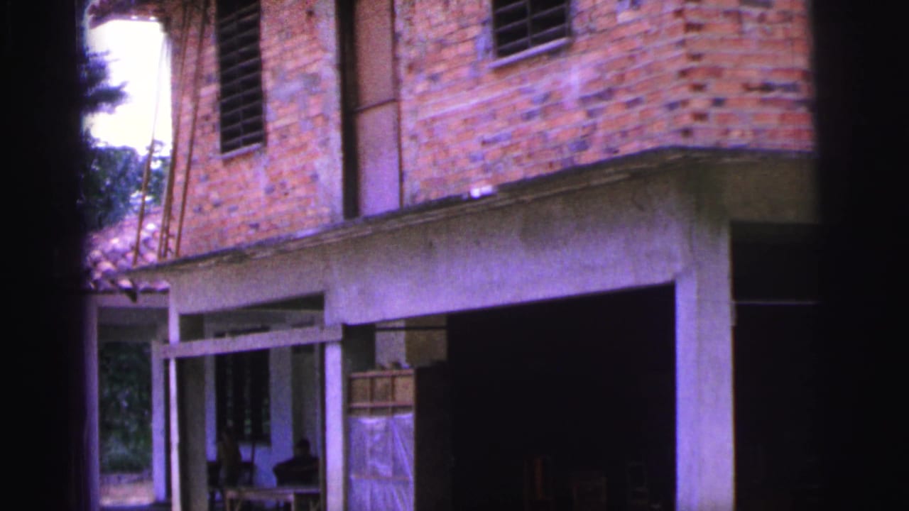 Closer view of the brick house facade, open doorway, concrete beam, and dark interior space.
