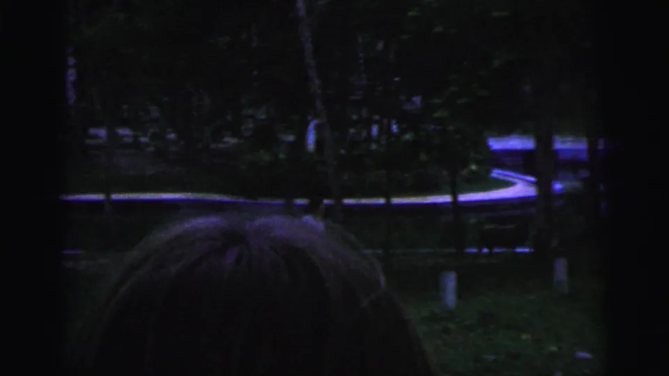 Dark 1967 Brazilian 8mm frame showing a blurry tree-lined path, reflective ground, and heavy film borders after the sign view.