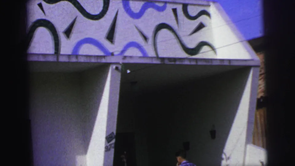 1967 Brazil 8mm frame showing a modernist white facade with blue and black wavy patterns over a dark entrance area.