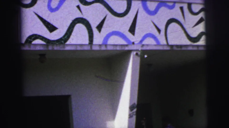 1967 Brazil home-movie frame of a patterned modernist facade with a partly visible person moving near the shaded doorway.