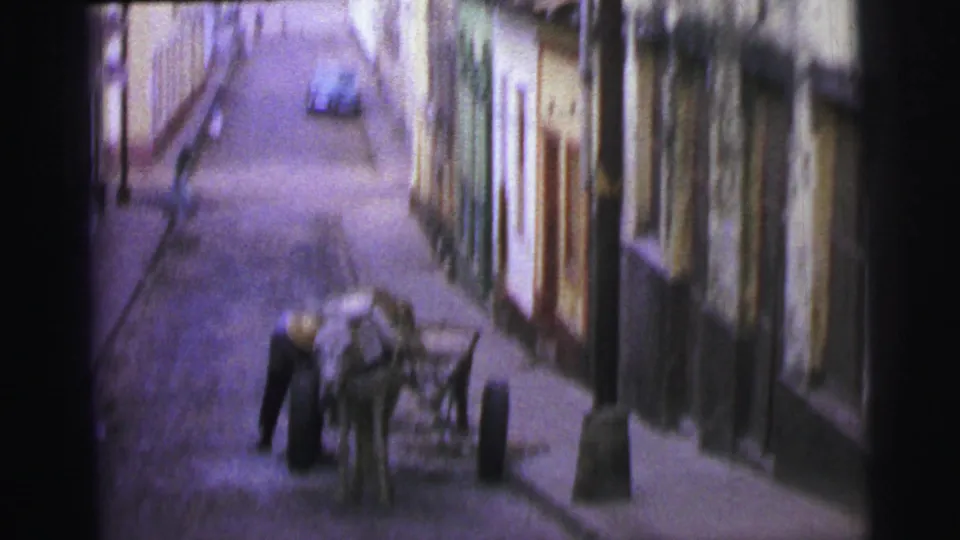 Soft 8mm frame from 1967 Brazil showing a man near a horse-drawn cart along a cobblestone street.