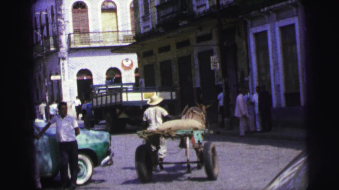 1967 Brazil street scene with a man leading a loaded horse cart past a green car, pedestrians, and arched building fronts.