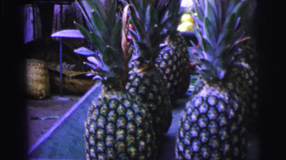 1967 Brazil 8mm frame showing pineapples with leafy crowns on an outdoor market stall.
