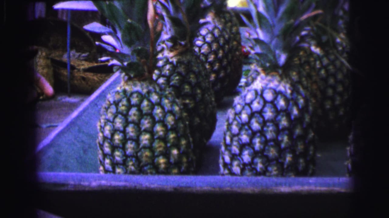 Pineapples sit on a stall with a person partly visible behind them.