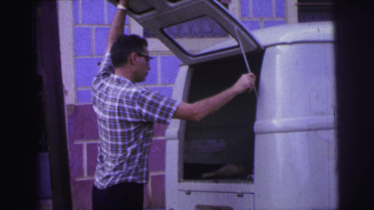 Man in plaid shirt opening the rear hatch of a white van.