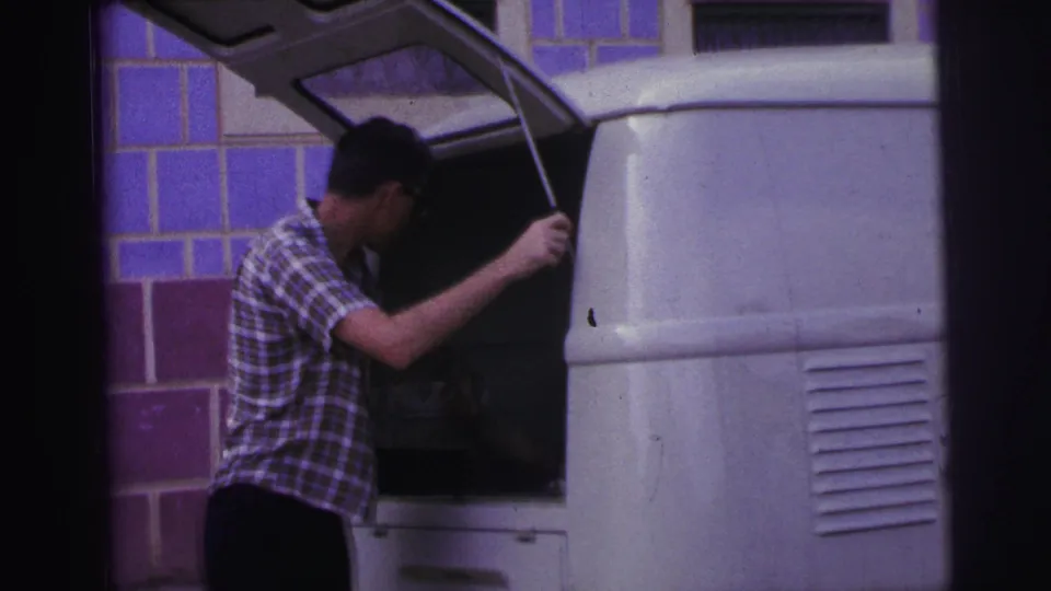 1967 Brazil frame showing a man beside a white van with the rear hatch raised, filmed in grainy 8mm color.