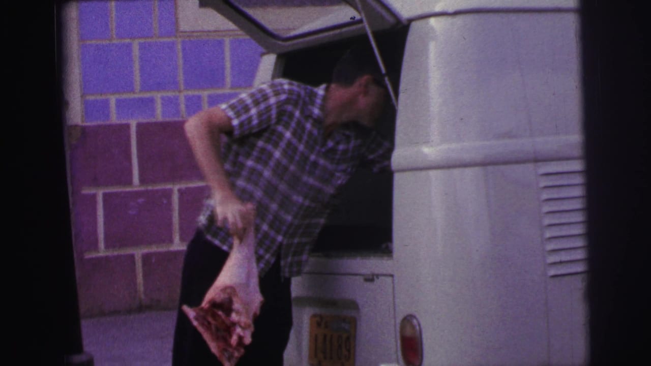 Man pulls a large piece of raw meat from the open rear of a white van.