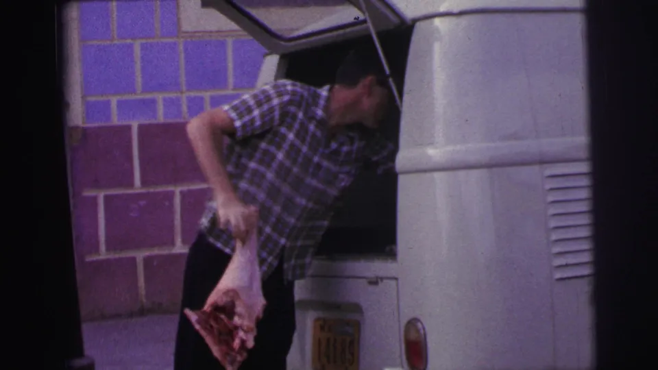 In 1967 Brazil footage, the man leans from the van holding a large piece of raw meat near the tiled wall.