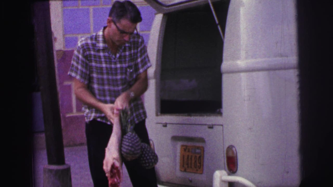 Man in a plaid shirt holds raw meat beside the open rear of a white van.