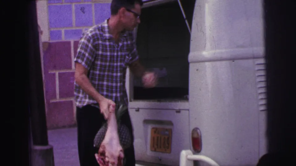 The man stands beside the open rear of the white van, holding raw meat as he appears to gesture toward the cargo area.
