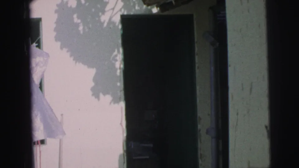 A 1967 Brazil home-movie frame with a dark doorway, pale wall, and a light-colored figure or garment at the entrance.