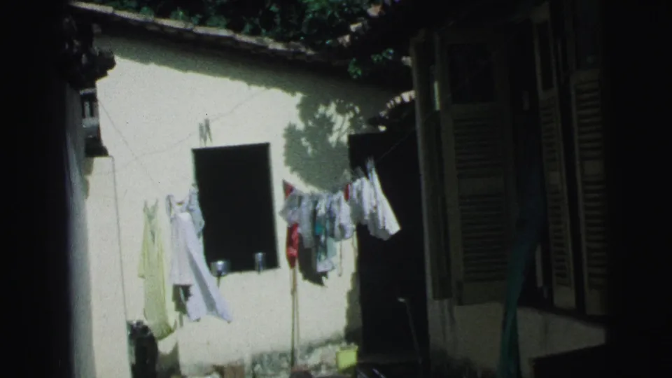 A 1967 Brazil home-movie frame of laundry moving on a clothesline in a residential courtyard with shutters and wall shadows.