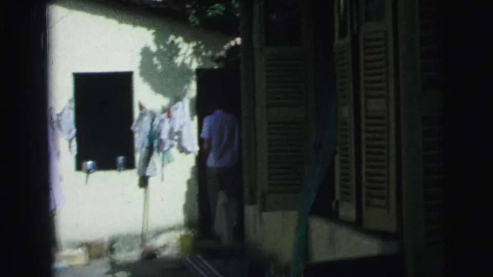 1967 Brazil home-movie frame with clothes drying on a courtyard line and a man partly visible near a doorway.
