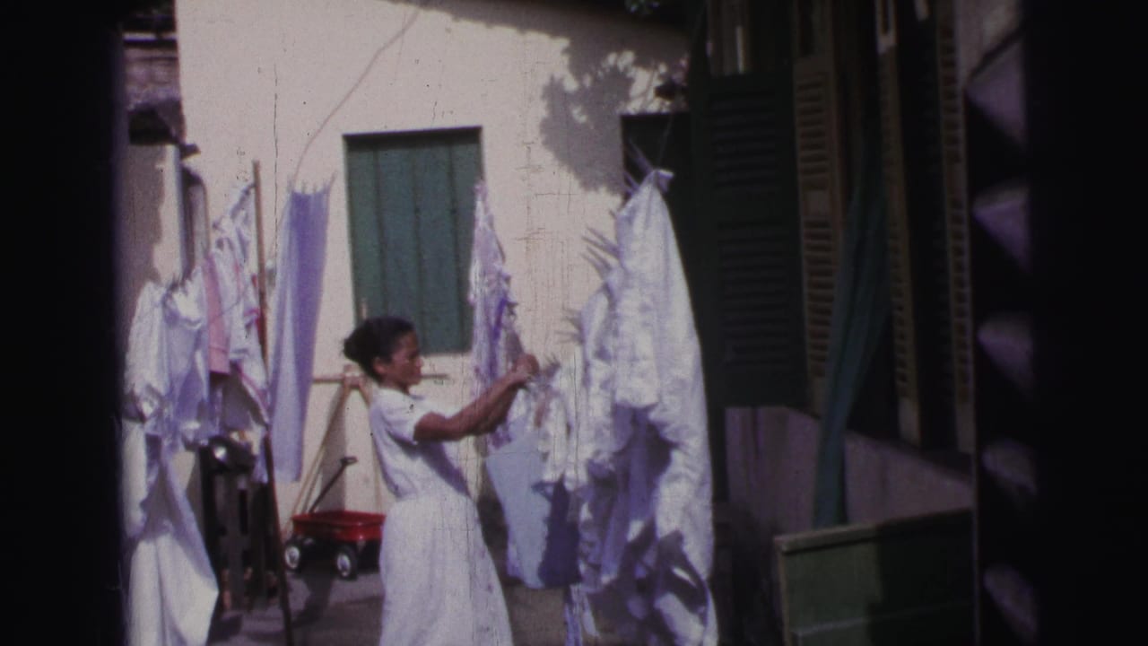 Woman in a white dress hanging laundry in a sunny courtyard.
