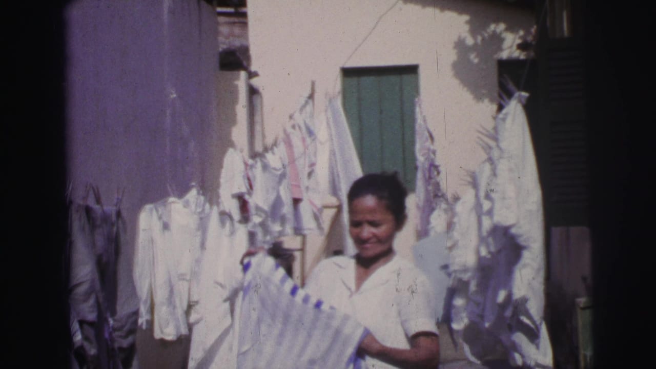 Woman in a white blouse folding a striped garment beside hanging laundry in a sunlit courtyard.