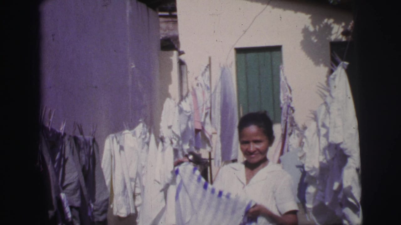 Woman holding laundry in a courtyard with white garments hanging around her.