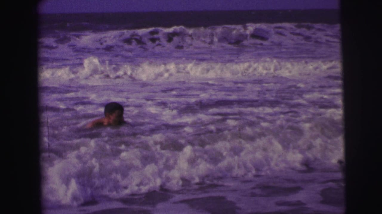 Swimmer partly submerged in foamy ocean waves beneath a dark horizon.