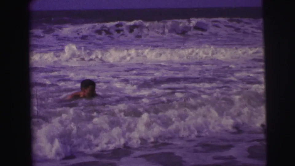 1967 Brazil 8mm frame showing a swimmer partly submerged as white surf rolls across a beach scene.