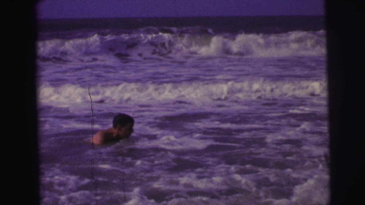 1967 Brazil 8mm frame of a swimmer in profile moving through foamy ocean water with larger waves behind.
