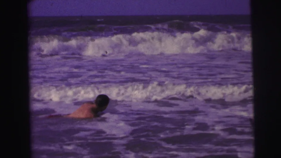 1967 Brazil 8mm frame with a swimmer low in the foreground water and a band of white surf behind him.