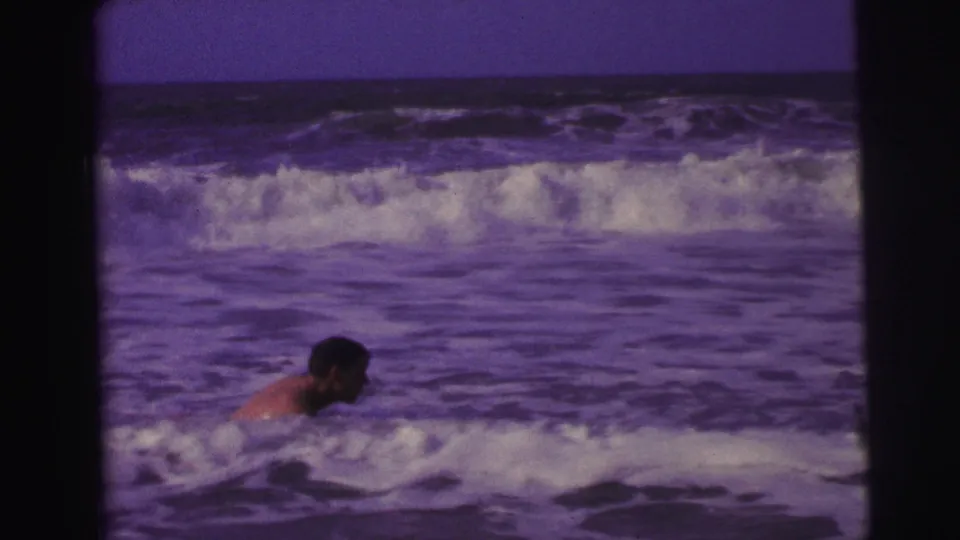 1967 Brazil 8mm frame showing a swimmer nearly submerged in rolling surf with white waves across the background.