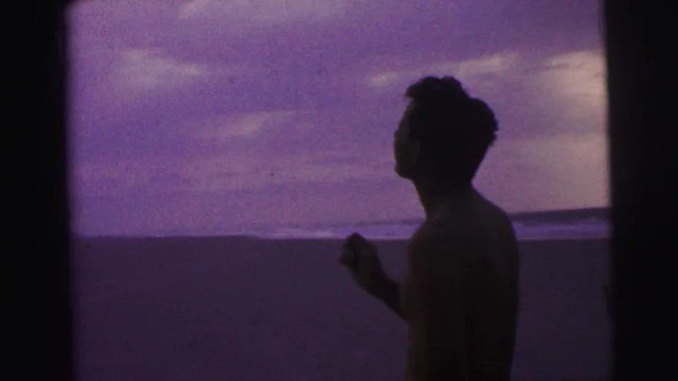 1967 Brazil 8mm frame with a dark side silhouette of a man near the beach facing the shoreline and distant surf.
