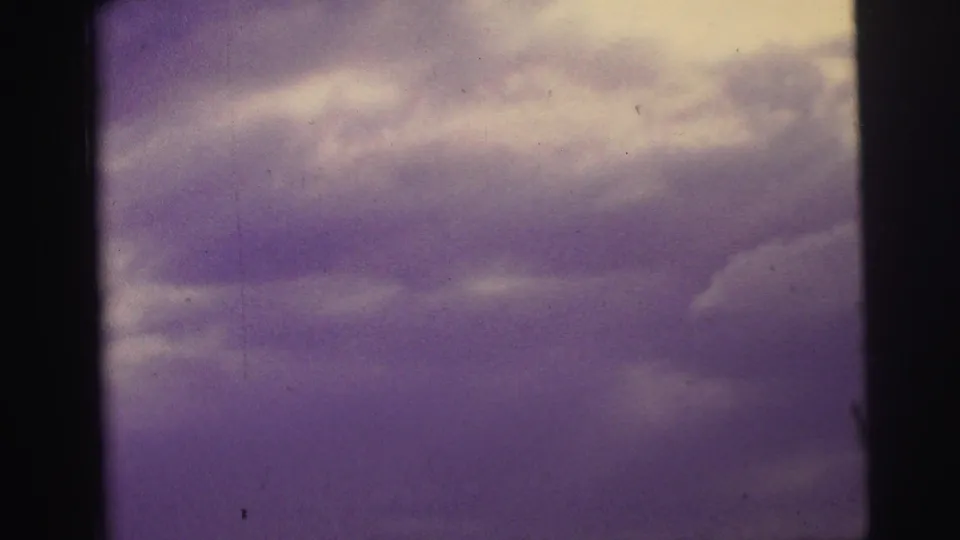 Purple-tinted sky and clouds fill the frame, with dark film edges visible from the 8mm scan.