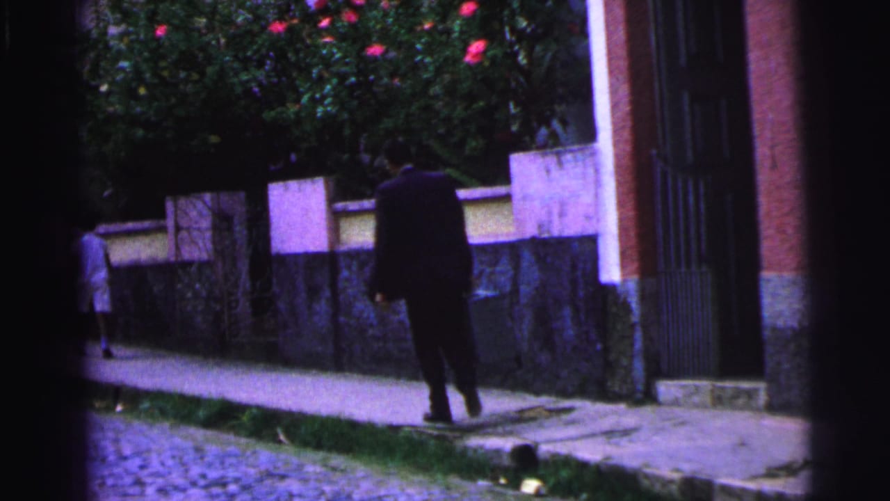 Suited man with a briefcase walks along a sidewalk beside a low wall.