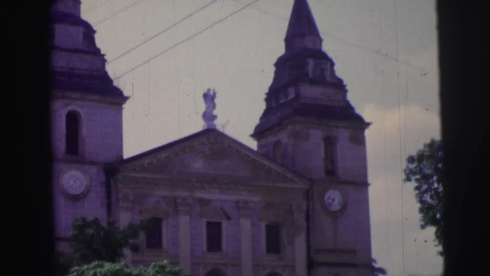 A Brazil church exterior with twin clock towers, a central statue or cross detail, and cloudy sky in soft 8mm color.