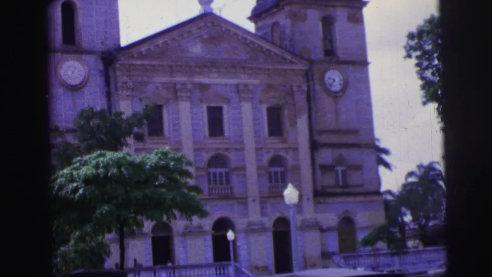 1967 Brazil 8mm frame with a slightly tilted church facade, tree canopy, arched entrance, and front balustrade.
