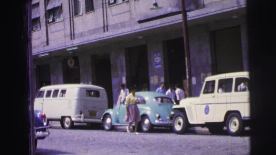 1967 Brazil street scene with a light blue compact car, white van, white utility vehicle, building frontage, and pedestrians nearby.