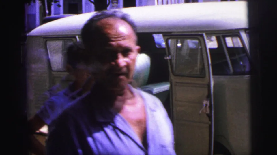 Adult man in a light shirt walks close to the camera, partly obscuring the 1967 Brazil dockside van and cargo crates behind him.