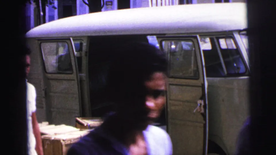 A person moves through the foreground near the open van, with crates and the dockside vehicle still visible in the 1967 Brazil home-movie frame.