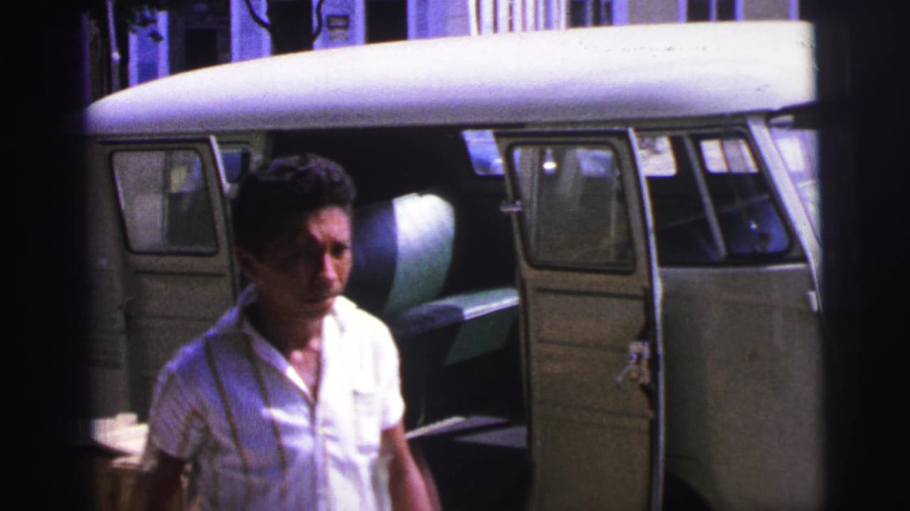Man in a white shirt stands beside an open two-tone van with crates nearby.