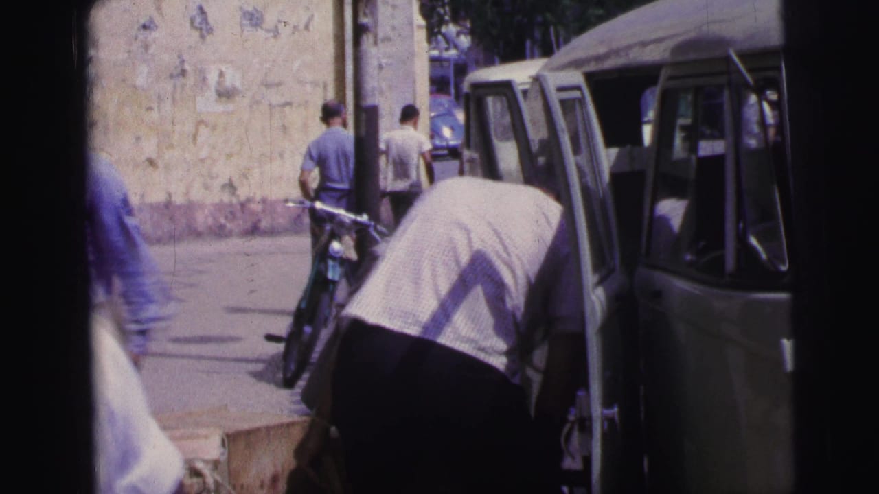 1967 Brazil street view with a man bending near a light Kombi-style van, a bicycle by a wall, and pedestrians in the background.