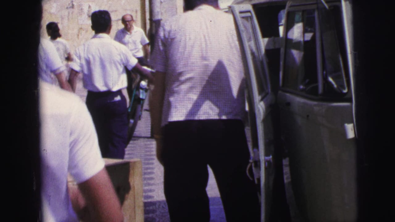 1967 Brazil home-movie frame showing men near an open van with a wooden crate on a busy sunlit street.