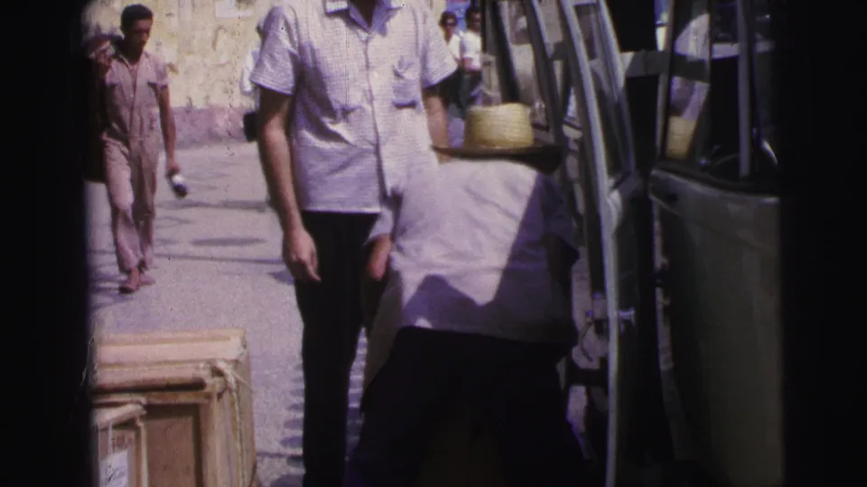 1967 Brazil street frame with a passerby in a white shirt and a straw-hatted man working beside an open van.