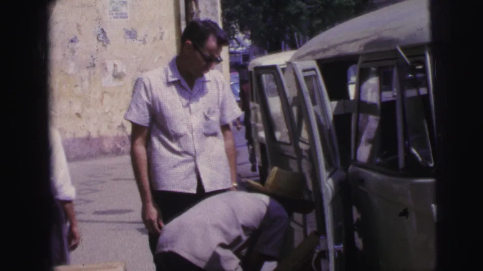 1967 Brazil street scene with a man in glasses standing by a van as another person loads items through the open side door.