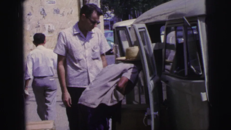 1967 Brazil 8mm frame with a straw-hatted man loading a van and another man standing nearby on a sunlit sidewalk.