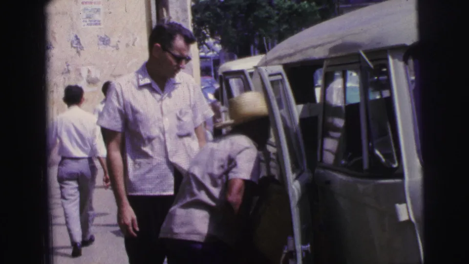1967 Brazil home-movie still of men beside a light green van, with one straw-hatted person bending into the open doorway.