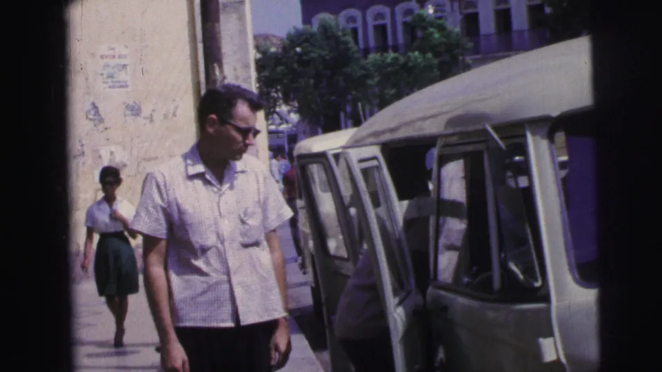 The man remains beside the van in bright daylight, with an adult figure near the vehicle and another pedestrian visible farther down the sidewalk.