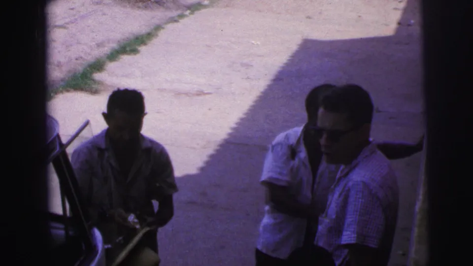 The final frame shows two adult men beside the van, partly in shadow, as the man in sunglasses turns toward another person near the vehicle.