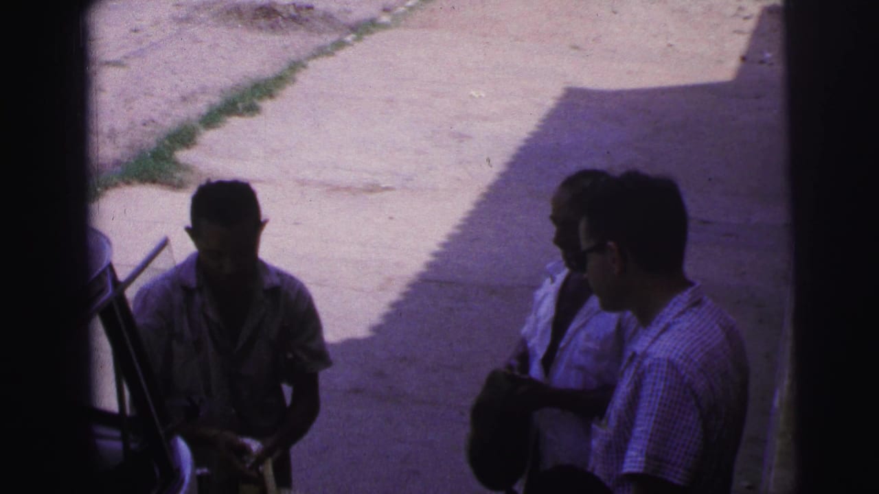 In this 1967 Brazil home-movie frame, one man in sunglasses faces another man who appears to hold a dark hat in the shade.